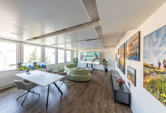 moderner, lichtdurchfluteter Büroraum mit Beratungstisch, Sofa und farbenprächtigen Bildern an der Wand